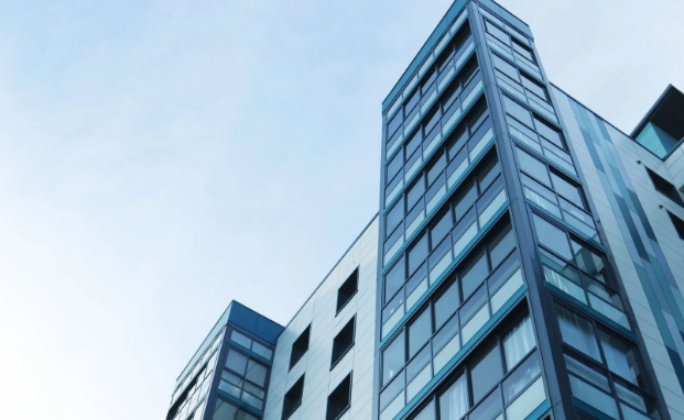 Edificio moderno de varios pisos con fachada de vidrio y metal bajo un cielo azul claro y despejado.